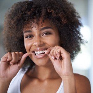 Woman smiling while flossing her teeth in bathroom