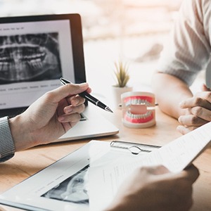 Dentist review paperwork with patient at desk with X-ray and model of teeth