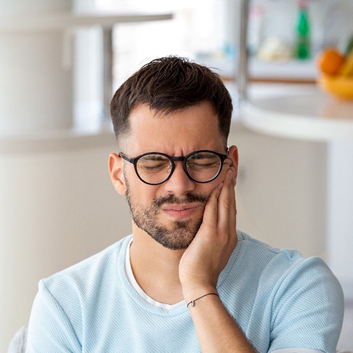 Man with glasses rubbing his jaw in discomfort