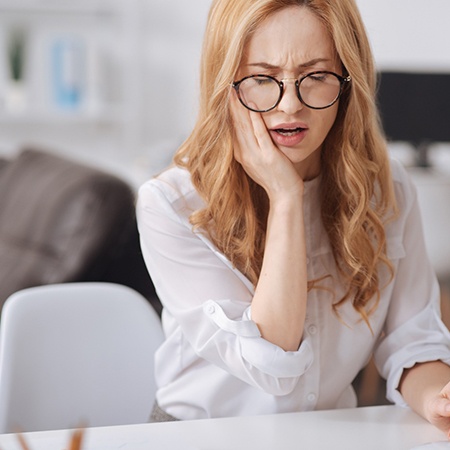 Woman in white shirt and glasses rubbing jaw