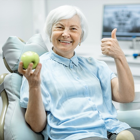 Woman smiling and holding an appeal after TeethXpress dental implant prosthetic restoration